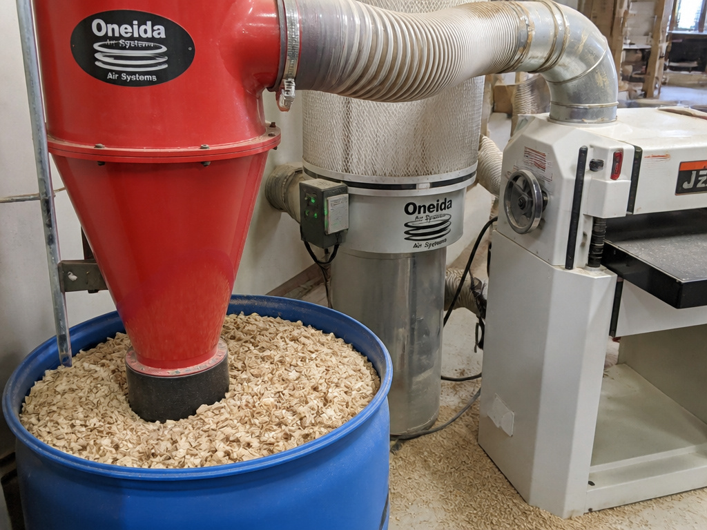 Two-stage cyclone dust collector filling a drum in a woodworking shop.